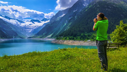 Fototapeta na wymiar Man takes a picture amazing view of Alpine lake Schlegeis