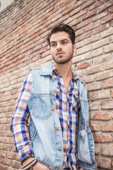 young casual man leaning on a brick wall