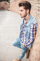 casual man leaning on a brick wal