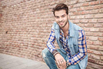 young man sitting near a brick wall