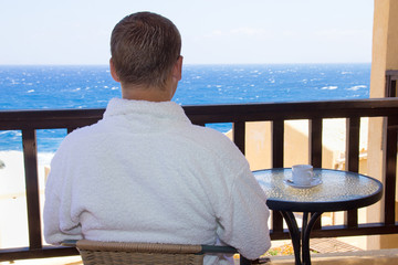 back view of man sitting on balcony with sea view - Powered by Adobe