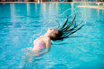 Девушка в бассейне брызгает длинными волосами