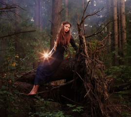 Beautiful witch sitting on a tree trunk in the forest
