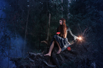 Beautiful witch sitting on a tree trunk in the forest