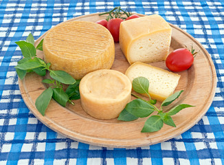 Round, circular cheeseboard with cheese on blue tablecloth. Orga