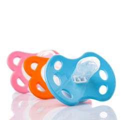 Orange, pink and blue pacifier over white background 