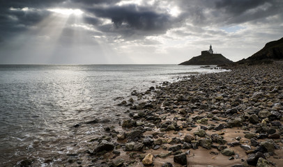 Lighthouse landscape with stormy sky over sea with rocks in fore
