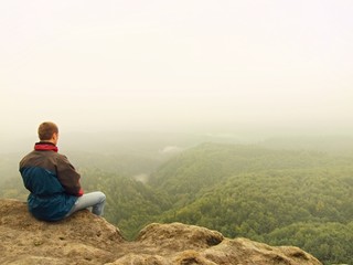 Fototapeta na wymiar Sad man sit on the peak of sandstone rock and watching down