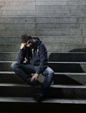 Young sad man crying in depression sitting on street stairs