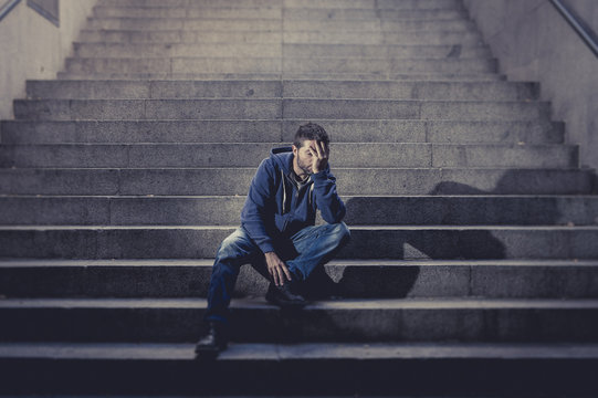 Young sad man depressed sitting on street stairs homeless