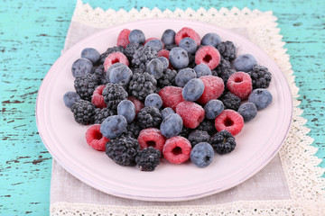 Iced berries on plate, on color wooden background