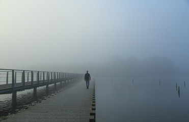 Man walking on a footbridge into the morning fog.