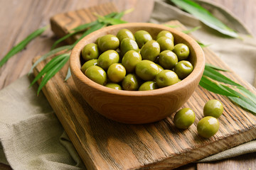Green olives in bowl with leaves on table close-up