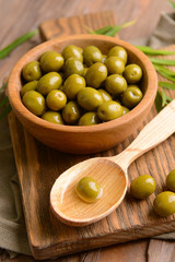 Green olives in bowl with leaves on table close-up