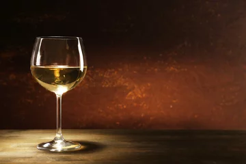 Photo sur Plexiglas Vin Goblet of white wine on wooden table on wooden wall background