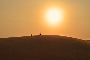 Silhouettes of sitting and talking friends on a sand hilll