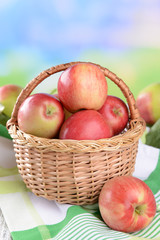 Sweet apples in wicker basket on table on bright background