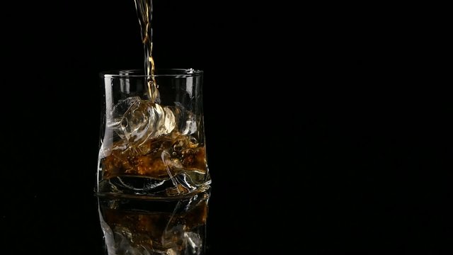 Whiskey being poured into a glass against black background. Long