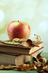 Apple with books and dry leaves on table on bright background