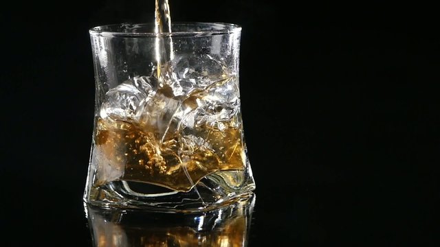 Whiskey being poured into a glass against black background.