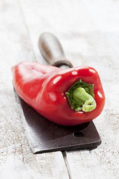 Ungarische Spitzpaprika, altes Hackmesser, weisser Holztisch