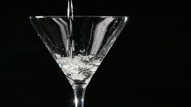 Martini being poured into a glass on black background. Slow