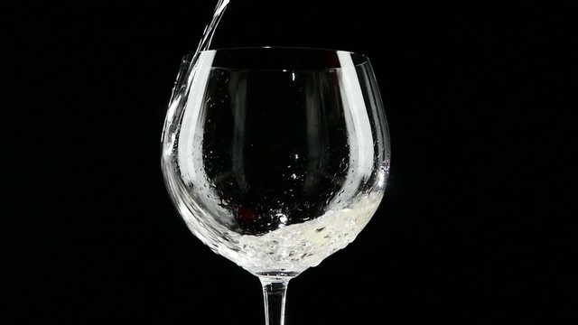White wine being poured into a glass of black background. Slow