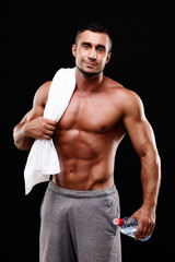 Fototapeta premium Handsome muscular sportsman holding towel and bottle with water