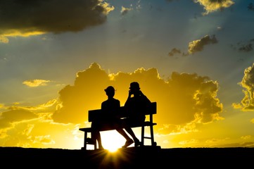 Young people sit on the bench with sunset on the background