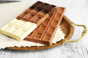 Chocolate bars on napkin, on tray, on wooden background