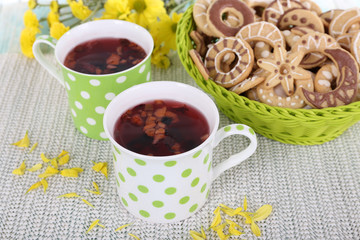 Two polka dot cups of tea with biscuits on fabric background