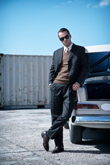 Retro fifties mafia fashion man standing next to open trunk of v