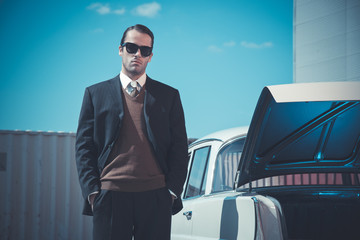 Retro fifties mafia fashion man standing next to open trunk of v