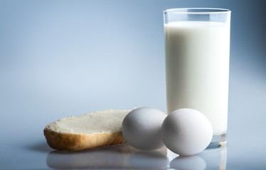 A glass of fresh milk, two eggs and bun with butter