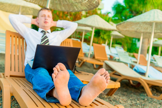 barefoot manager on a sun lounger with a laptop