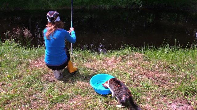 Woman fishing on lake shore and cat cath fish from bucket  water
