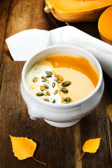 Pumpkin soup in white plate on wooden table with pumpkin seeds.
