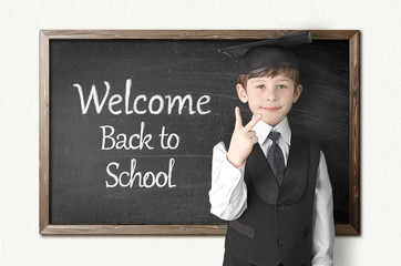 Cheerful little boy on blackboard. Looking at camera