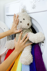Woman loading fluffy toy in the washing machine