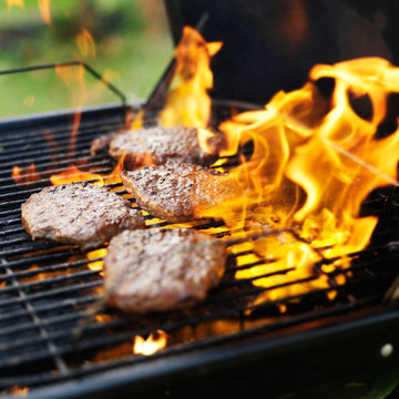 hamburgers being grilled with flames
