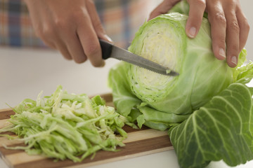 Woman cuts cabbage on cutting board in kitchen - Powered by Adobe