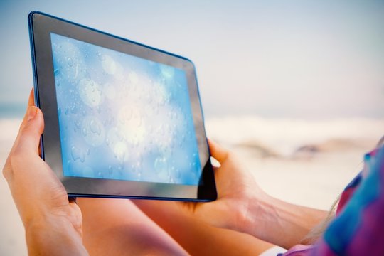 Woman sitting on beach in deck chair using tablet pc
