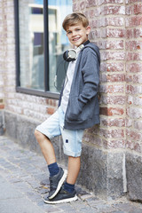 Young boy wearing headphones against wall, portrait.