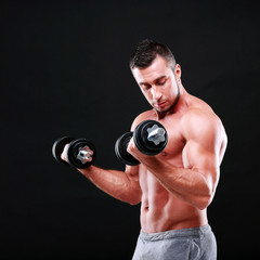 Fototapeta na wymiar Portrait of a sportsman lifting dumbbells over black background