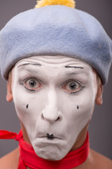 Portrait of young male mime with white face, grey hat showing em