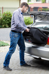 Man putting luggage into car trunk