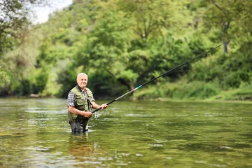 Fototapeten Ein älterer Mann, der an einem sonnigen Tag in einem Fluss fischt © Ljupco Smokovski