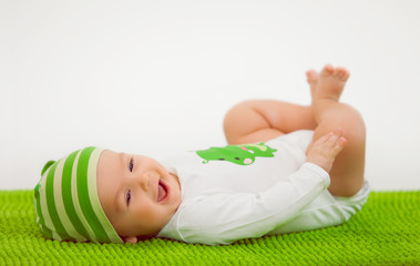 Smiling baby in a hat lying on the green soft carpet
