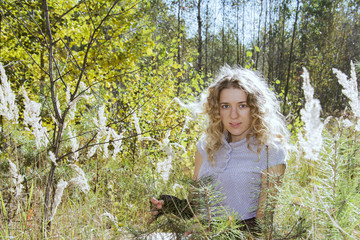Fototapeta na wymiar In the autumn forest on a glade curly girl in tall grass in the