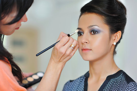 Pretty young woman applying makeup by makeup artist